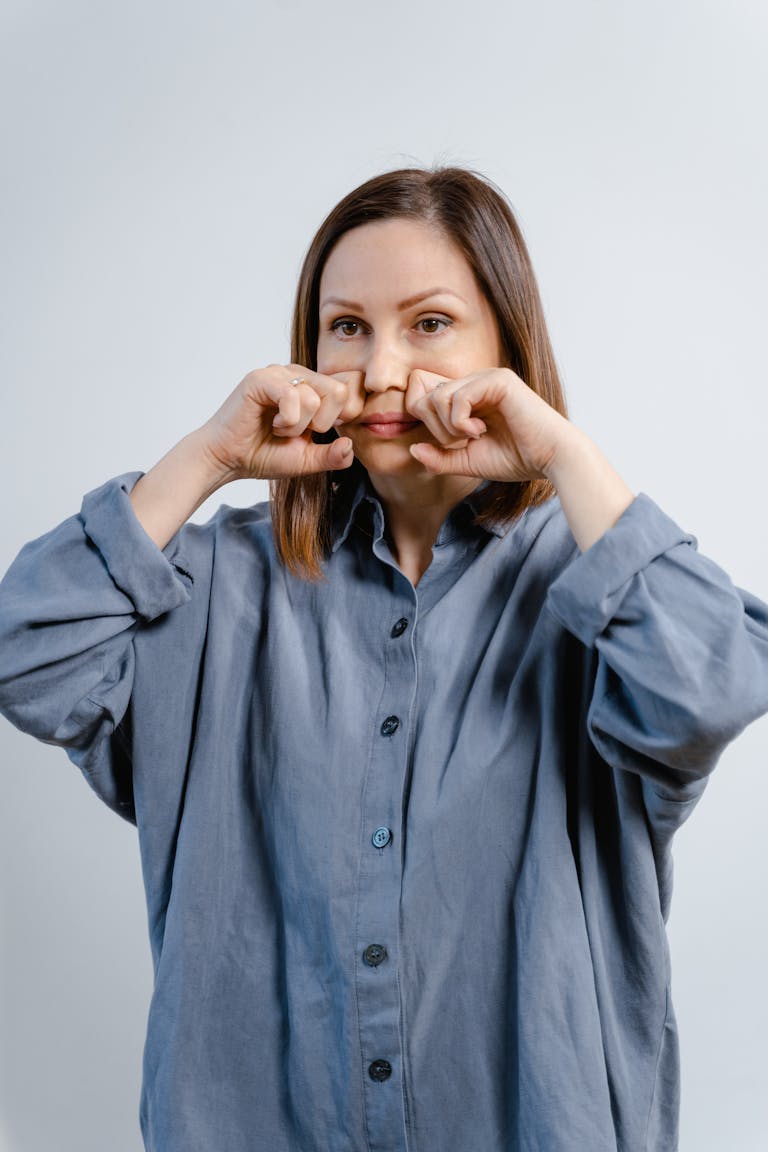 A young woman indoors demonstrating a facial exercise for wellbeing and skin care routines.